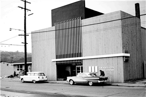 A windowless building with two 1960s era cars parked in front